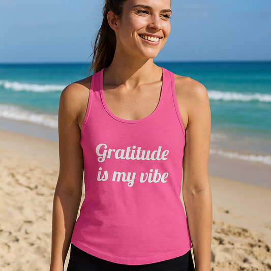 Woman wearing a bright pink tank top on the beach with the quote “Gratitude is my vibe” printed on the front.