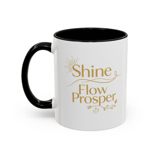 White ceramic mug with black handle and interior, featuring gold “Shine, Flow, Prosper” affirmation text – by Druvs.